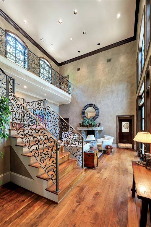 This view of the family room showcases the incredible ceiling height, multitude of arched windows that flood this space with natural light, and grand staircase with intricate wrought-iron railings. The archway pictured on the right leads to a back corridor, providing access to a powder bath along with exterior access to the summer kitchen area.