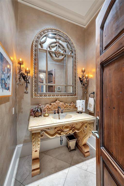 One of three powder baths, this stunning space is situated between the formal living room and kitchen. Features include a hand-carved solid marble vanity complemented by an arched gilded mirror and two decorative wall sconces from France, along with travertine tile flooring, 11” baseboards, double crown molding, recessed lighting, oil-rubbed bronze faucet and hardware, and a Toto toilet.