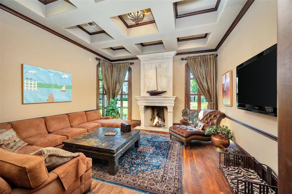 The study boasts a coffered ceiling with wood-stained crown molding, a limestone wood-burning fireplace and overmantel, and three floor-to-ceiling windows with custom draperies. Additional highlights include waxed hardwood flooring, 11” wooden baseboards, wood-stained chair railing, recessed and art lighting, a glass bowl light fixture with bronze accents, and surround sound.