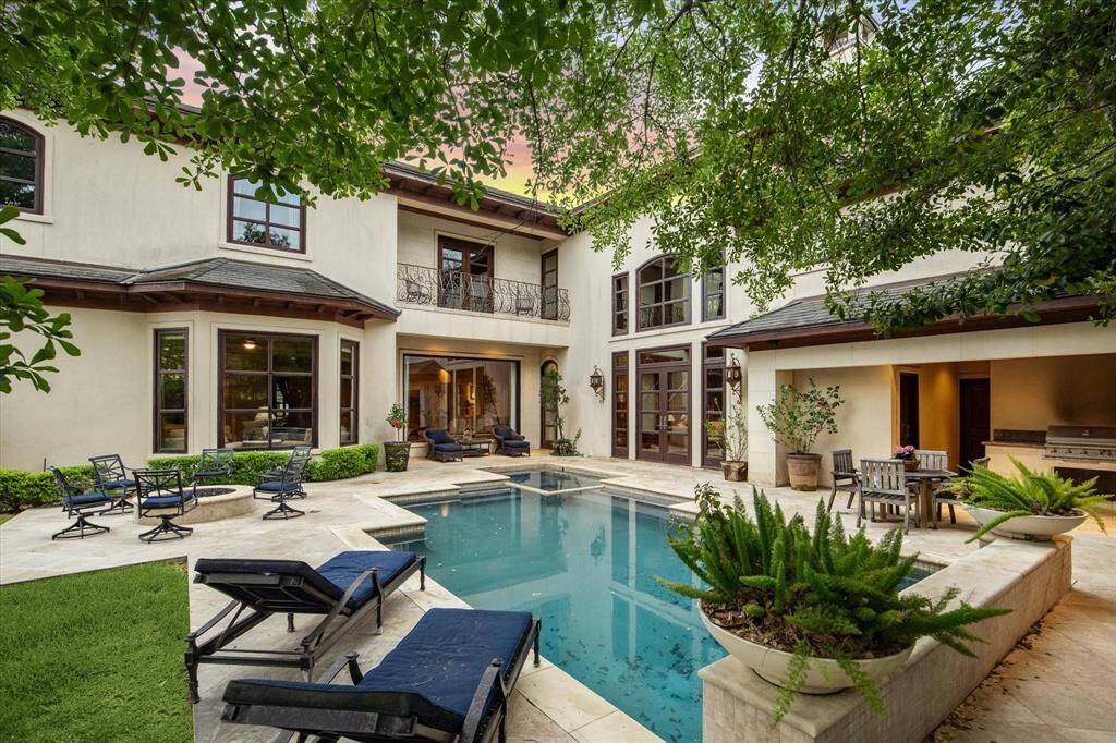 The resort-style backyard includes a sparkling saltwater pool with waterfall, spa, built-in firepit, travertine tile patio areas, and a summer kitchen with a built-in grill, perfect for entertaining. Large windows and French doors enhance the connection between indoor and outdoor living.