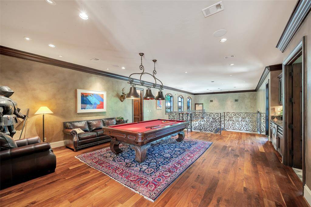 The expansive gameroom located on the second floor has access to a powder bath, exterior balcony, and children’s gameroom. Highlights include hardwood flooring, 11” baseboards, faux painted green walls, wooden crown molding, and bronze 3-pendant chandelier. The wrought-iron stair railings overlook and provide access to the downstairs family room.