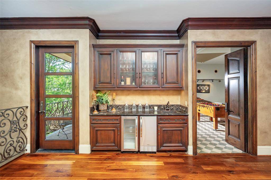 The gameroom also features a wet bar with custom wooden built-ins, glass-front upper cabinets, undercabinet lighting, black marble countertop, hammered bronze bar sink with a bronze faucet, and stainless Viking beverage fridge and ice maker.