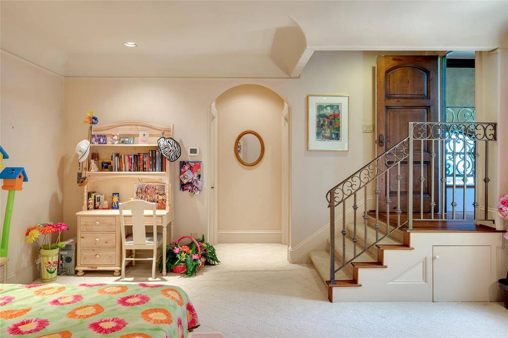 This view of the secondary bedroom highlights the whimsical entrance through a paneled wooden door leading to carpeted stairs with a wrought-iron handrail. The open archway leads to a large walk-in closet and spacious en-suite bathroom.