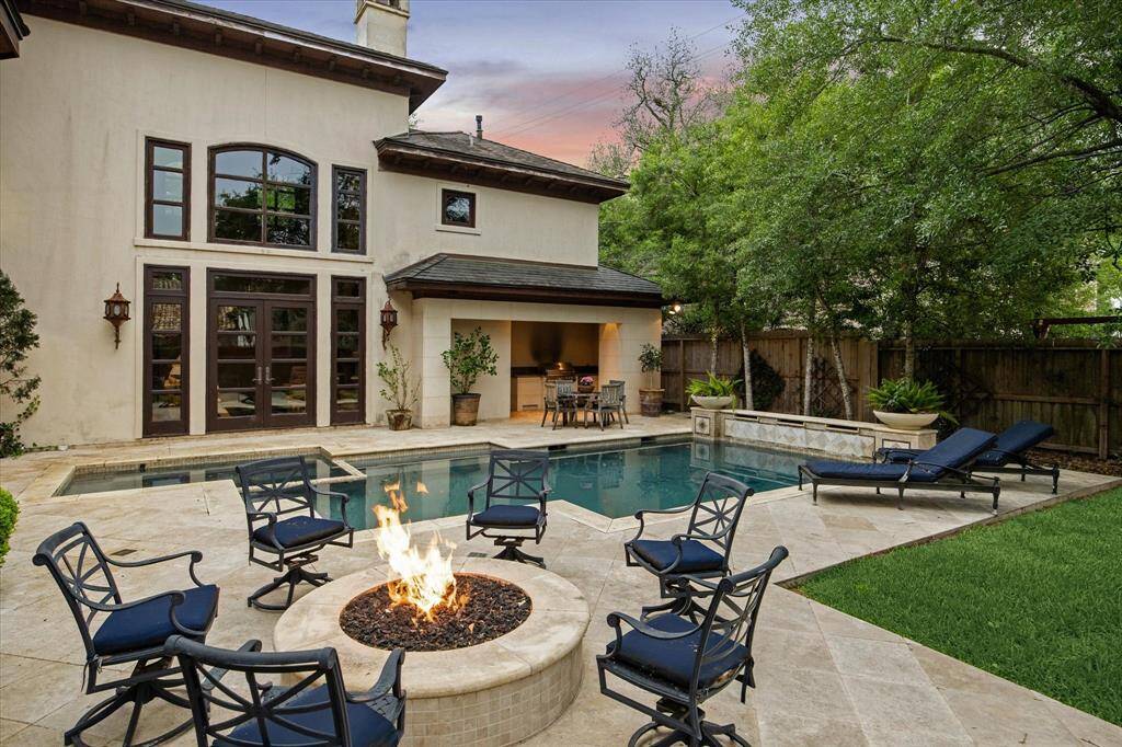 This view of the backyard showcases multiple seating areas and a fire pit that provide ample space for outdoor relaxation and entertainment, all nestled amidst lush greenery.