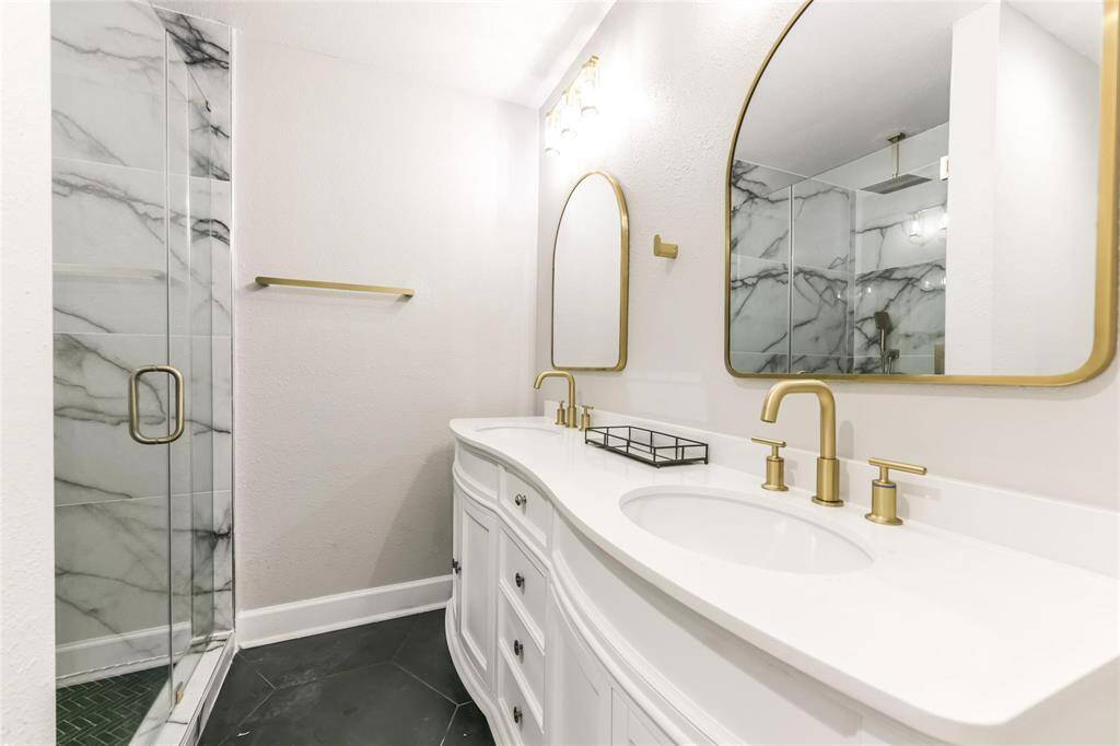 Ensuite bathroom for primary bathroom includes his & hers sinks with touches of gold finish and a modern vanity all resting on smooth white outlined black tiling