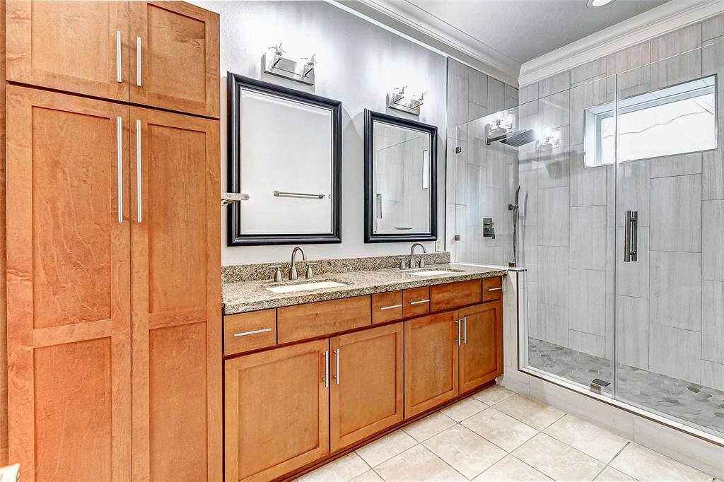 This primary bathroom boasts a spa-like ambiance with dual vanities featuring granite countertops and ample cabinet storage in gorgeous wood tones.