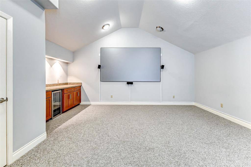 This versatile living area is perfect for entertainment, featuring a spacious layout with neutral carpeting and a vaulted ceiling.