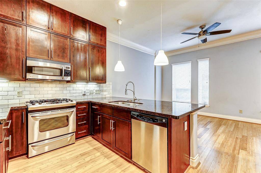 The granite countertops provide ample workspace, with a large peninsula island housing a double sink and a modern pull-down faucet. Light hardwood floors and pendant lighting complete the space, giving it a bright and inviting feel.