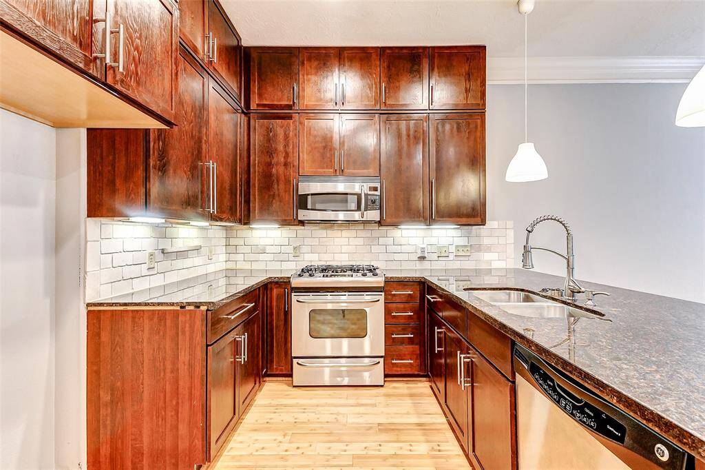 This kitchen also features rich wood cabinetry that extends all the way up to the ceiling complemented by sleek stainless steel appliances, including a built-in microwave and gas range. The subway tile backsplash adds a classic touch and dimension, while under-cabinet lighting enhances functionality and ambiance.