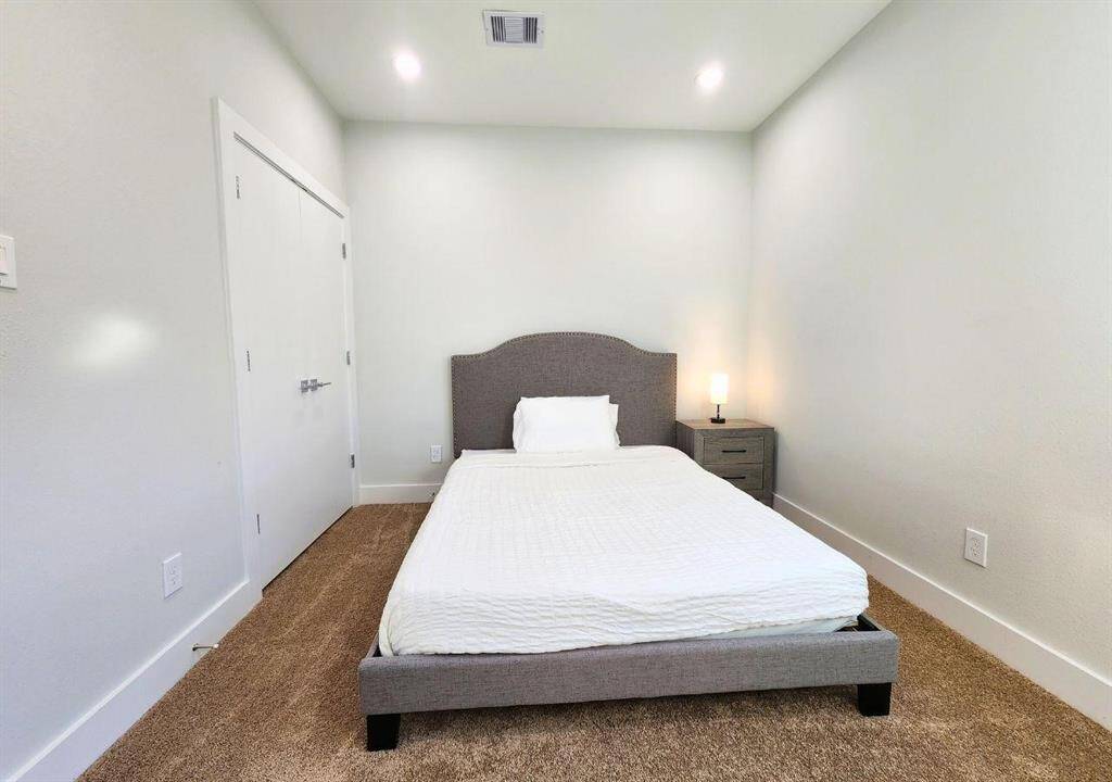 This bedroom features minimalist design with a neutral color palette, and soft carpeting.