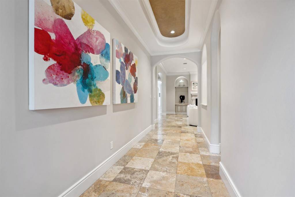This elegant entryway welcomes with a accented tray ceiling, arched openings, and Travertine flooring that sets a refined tone for the home.