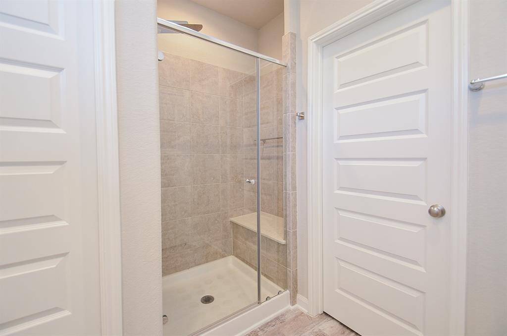 Step into this next well-appointed bathroom showcasing a modern glass-enclosed shower with tiled walls and a convenient built-in bench.