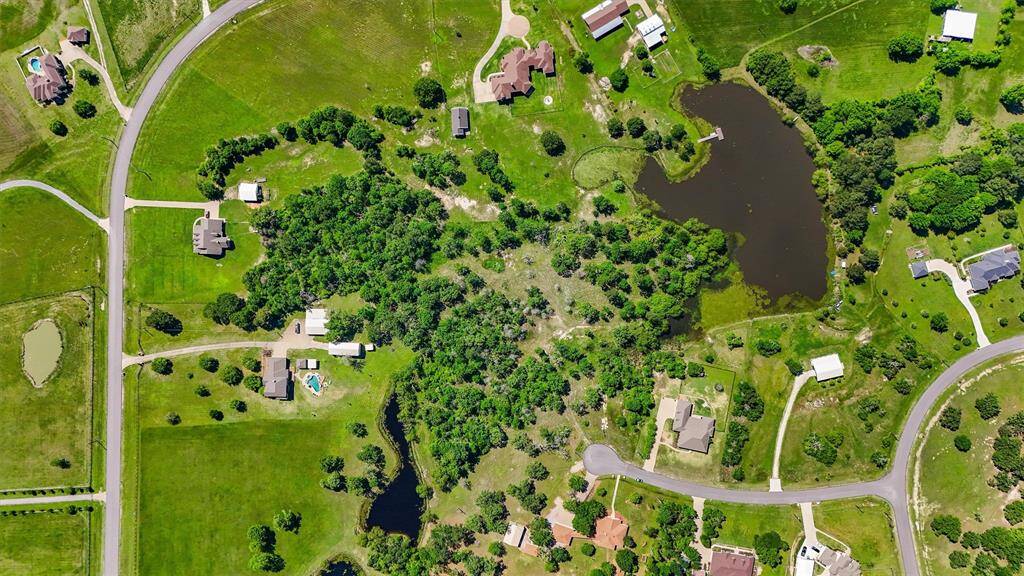 This aerial photo showcases a spacious property featuring multiple homes surrounded by lush greenery and trees. It includes open fields, and well-maintained roads in a tranquil, rural setting. Ideal for those seeking privacy and nature.