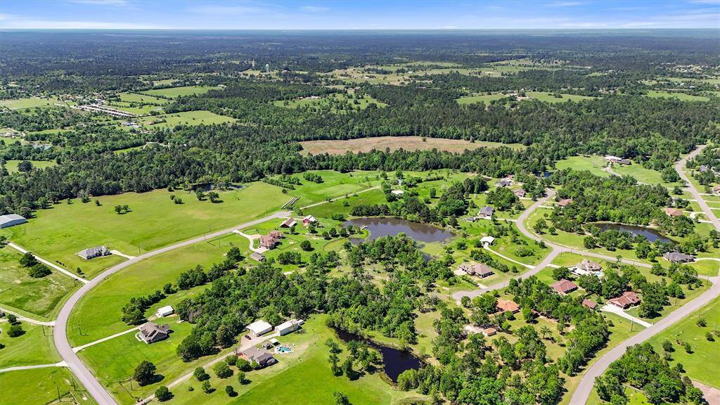 This aerial photo showcases a picturesque suburban area with spacious green lots, winding roads, and scattered houses. The landscape is lush, with several small ponds and dense woodland areas, offering a serene and private setting ideal for homebuyers seeking tranquility and natural beauty.