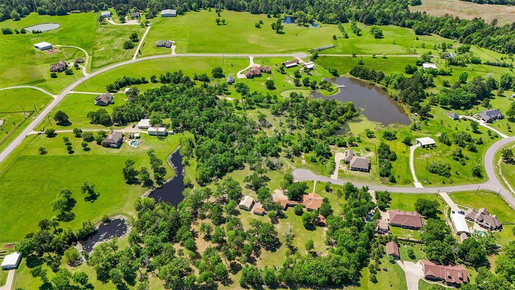 Scenic aerial view of a spacious rural neighborhood featuring lush greenery, multiple ponds/lake, and large properties with ample land. Ideal for those seeking tranquility and natural beauty.