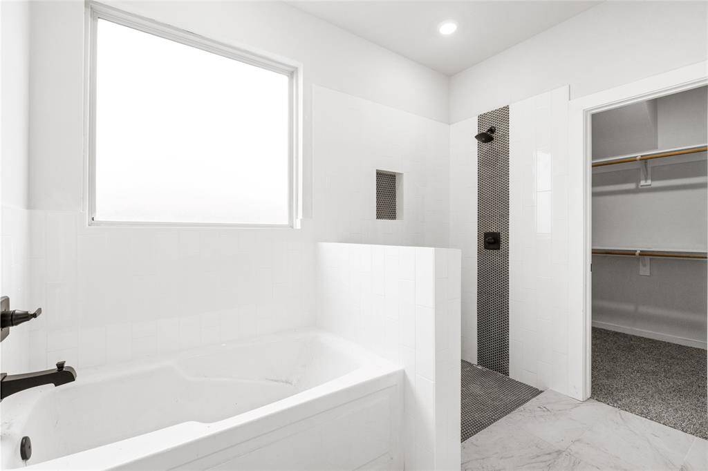 This bathroom features a modern design with a spacious tub, a sleek walk-in shower with stylish tiling, and an adjoining walk-in closet, all illuminated by natural light.