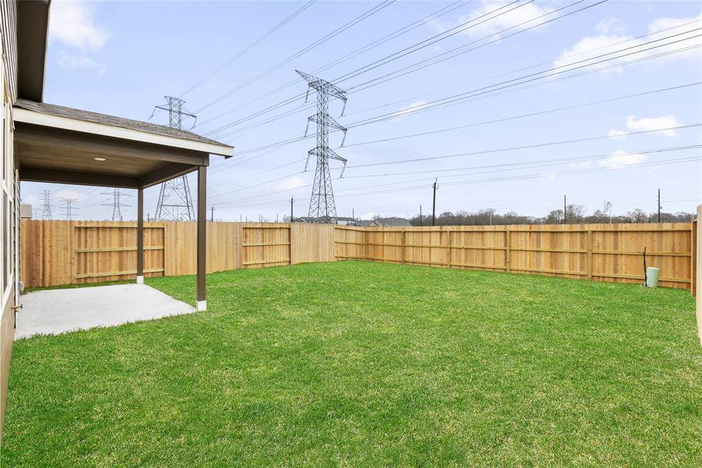 Spacious backyard with a well-maintained lawn, wooden fencing for privacy, and a covered patio area. Ideal for outdoor activities and relaxation.