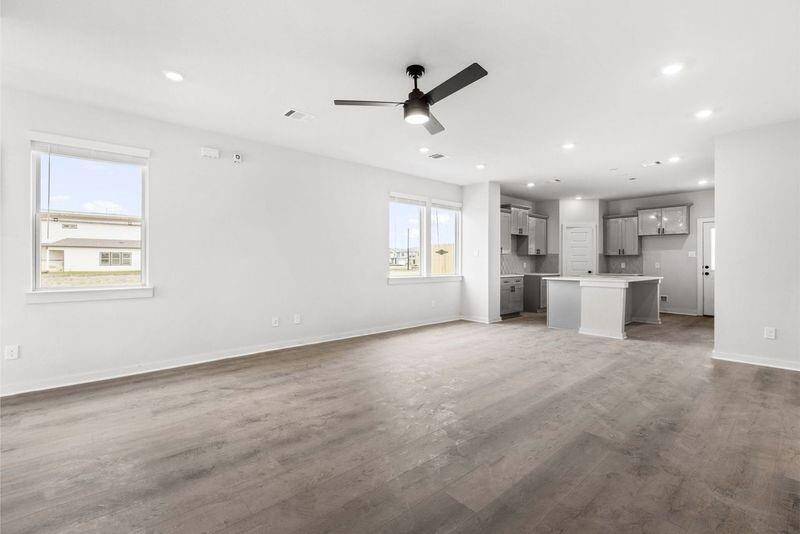 This photo showcases a spacious, open-concept living area with modern finishes. It features large windows for natural light, neutral walls, and wood-style flooring. The kitchen includes a central island and sleek cabinetry, creating a bright, inviting space perfect for entertaining.