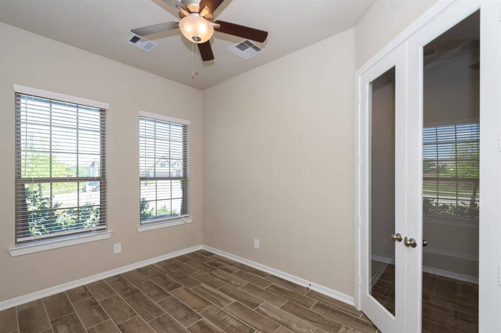 Bright front room with two large windows, wood-look tile flooring, a ceiling fan, and double glass doors. Ideal for an office or cozy reading nook.