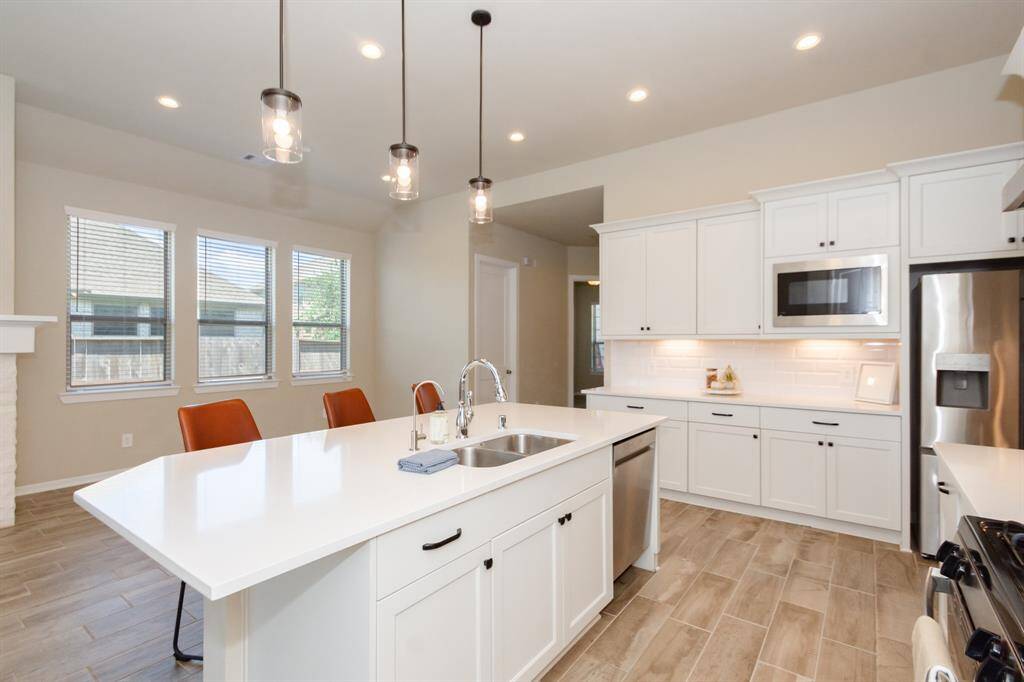 This bright, modern kitchen features a large island with a sink and seating, stainless steel appliances, and white cabinetry with ample storage. Recessed lighting and pendant lights illuminate the space, while large windows offer natural light.