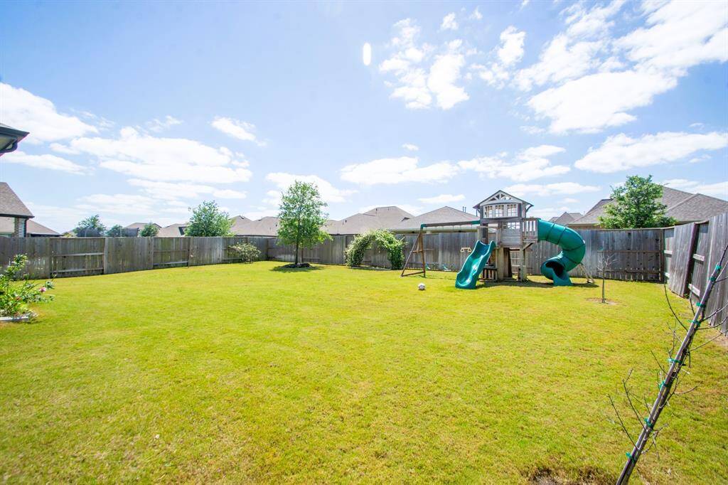 Spacious backyard with a well-maintained lawn, fenced perimeter, and a children's playset, offering a great space for families.