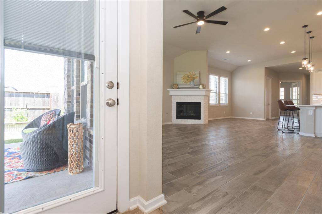 This photo showcases a bright, open-concept living area with modern tile flooring, a cozy fireplace, and ample natural light. The adjacent kitchen features a breakfast bar with stylish pendant lighting. A glass door leads to a patio for outdoor relaxation.