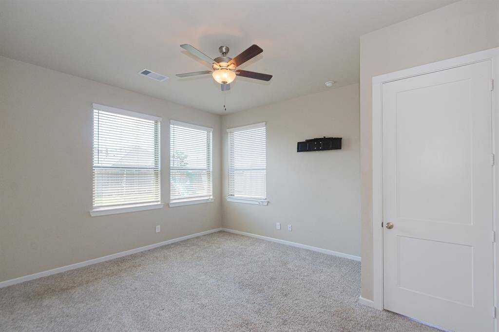 Bright and spacious primary bedroom with neutral walls, carpeted flooring, and large windows for natural light. Features a ceiling fan and a closet, ideal for a bedroom or home office.