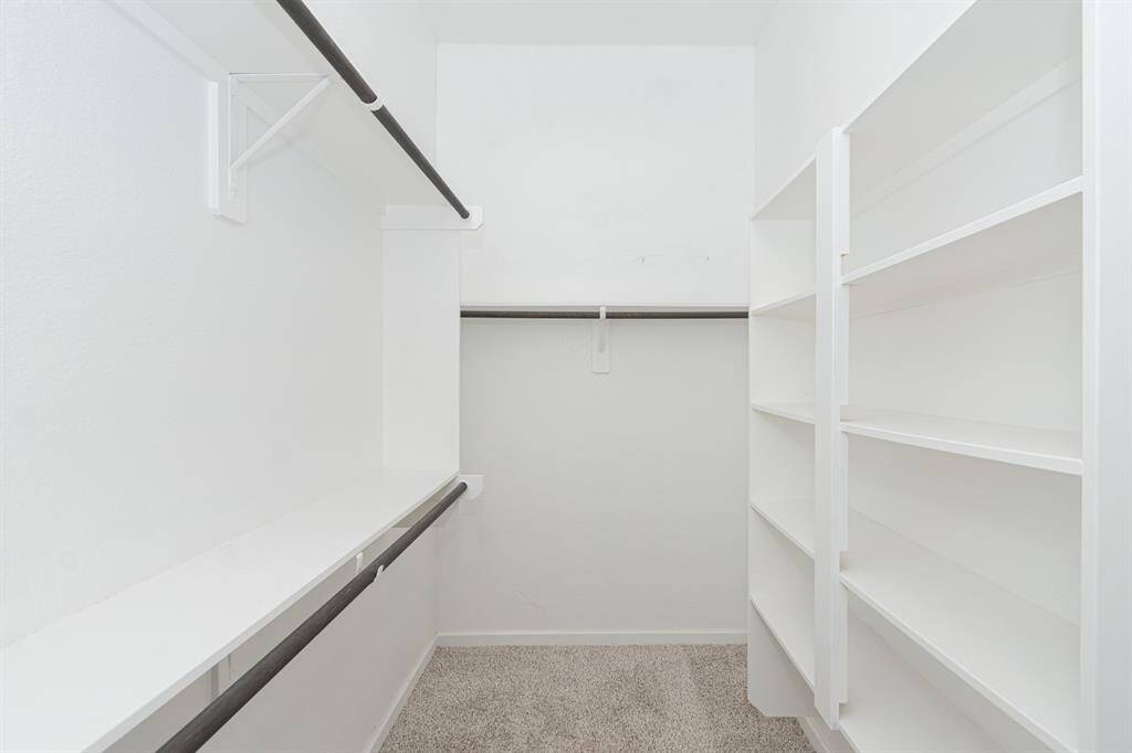 Another spacious walk-in closet with multiple shelves and hanging rods, featuring a clean, white finish and carpeted floor.