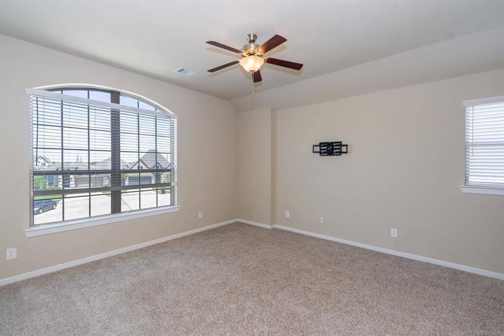 This game room features a neutral color palette, plush carpeting, and ample natural light from large windows. It includes a ceiling fan and offers a spacious, versatile area ideal for various uses.