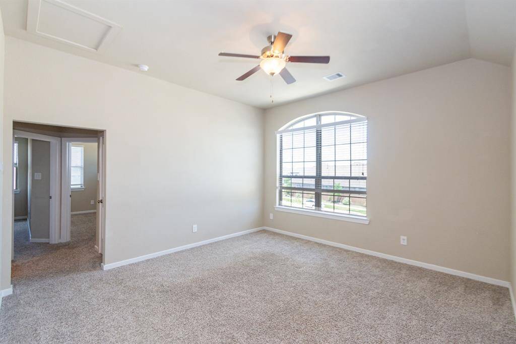 Bright, spacious game room with neutral walls and carpet, features a large arched window and ceiling fan. Two bedrooms, full bathroom and storage closet are visible through an open doorway.
