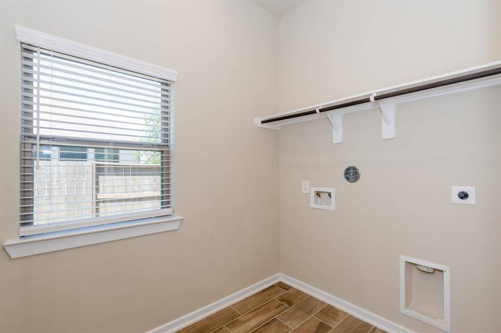 This bright laundry room has a window, tile flooring, hookups for a washer and dryer, and a storage shelf.
