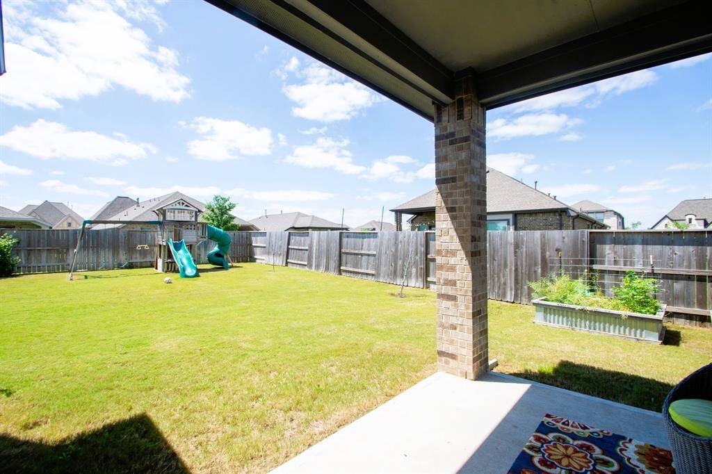 Spacious backyard with a covered patio, perfect for outdoor activities. Features a children's playset and a raised garden bed, surrounded by a wooden privacy fence.