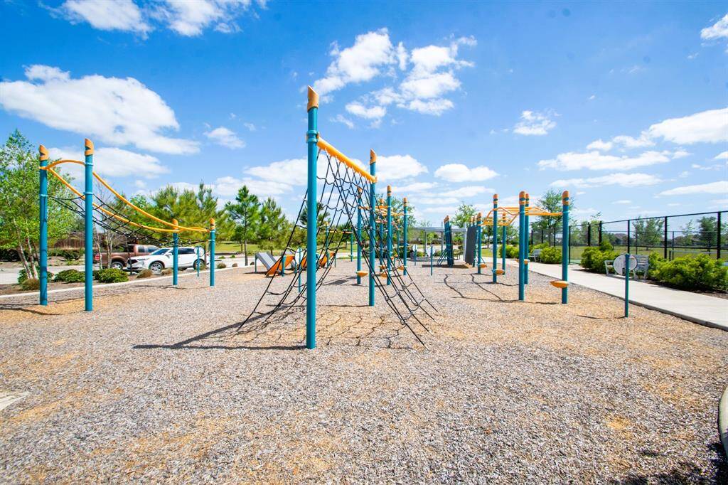 A modern playground with climbing structures and slides, set in a well-maintained park area. The space is surrounded by greenery and offers a bright, inviting atmosphere, perfect for families.