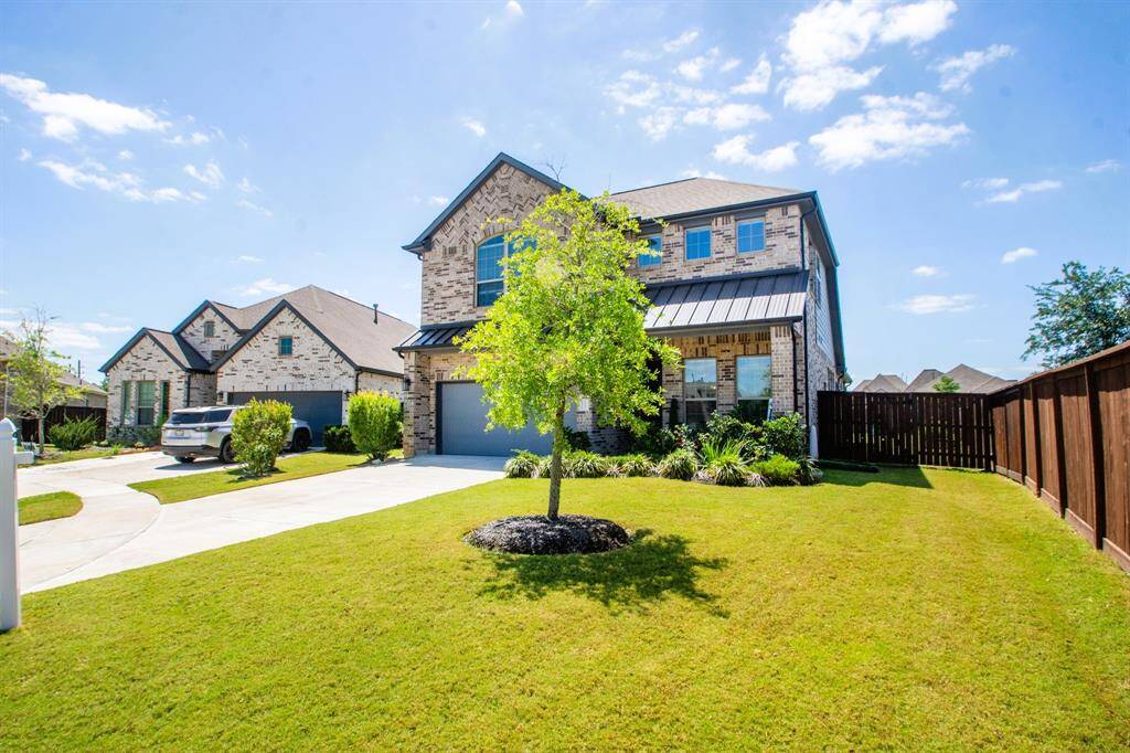 This charming two-story brick home features a well-maintained yard with a tree and a spacious driveway leading to a two-car garage. The property is enclosed by a wooden fence, offering ample privacy and a welcoming curb appeal.