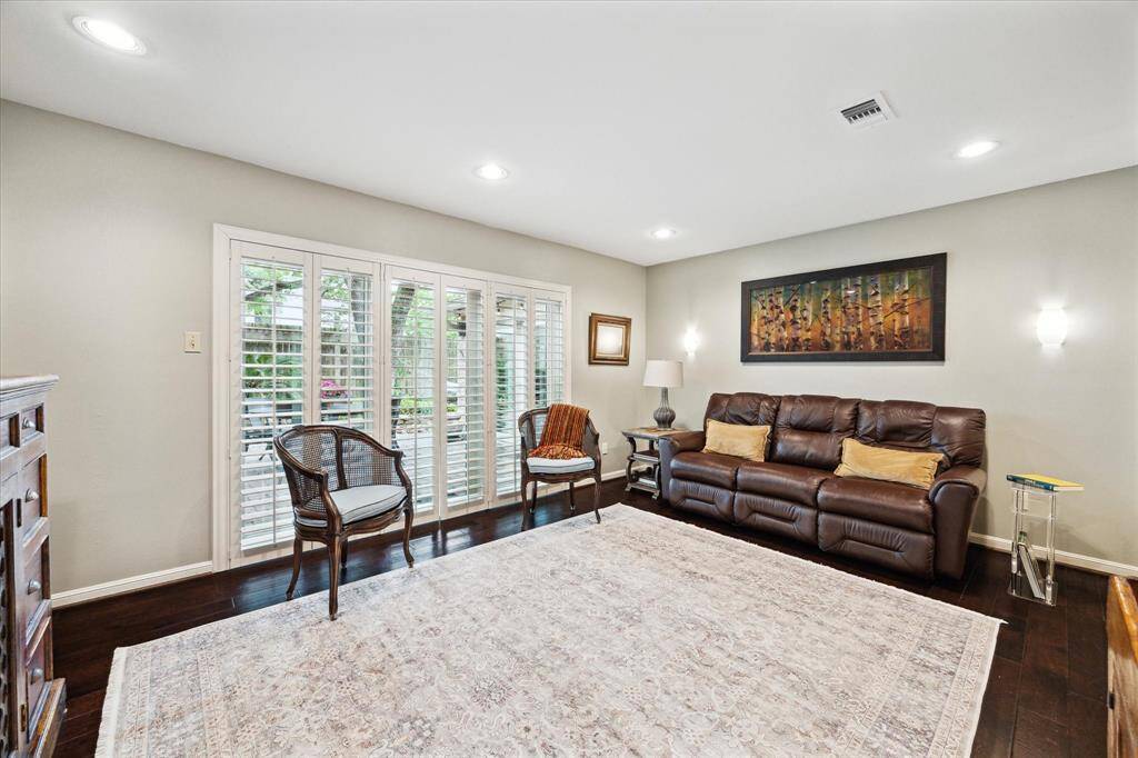 This inviting living room features dark hardwood floors and ample natural light from large windows with shutters. It is just off of the front entry. Recessed lighting and neutral paint give this room a peaceful feel