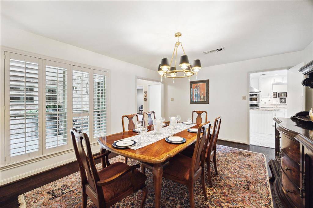 Elegant dining room with hardwood floors and a stylish chandelier, large windows with plantation shutters, and access to a bright kitchen.