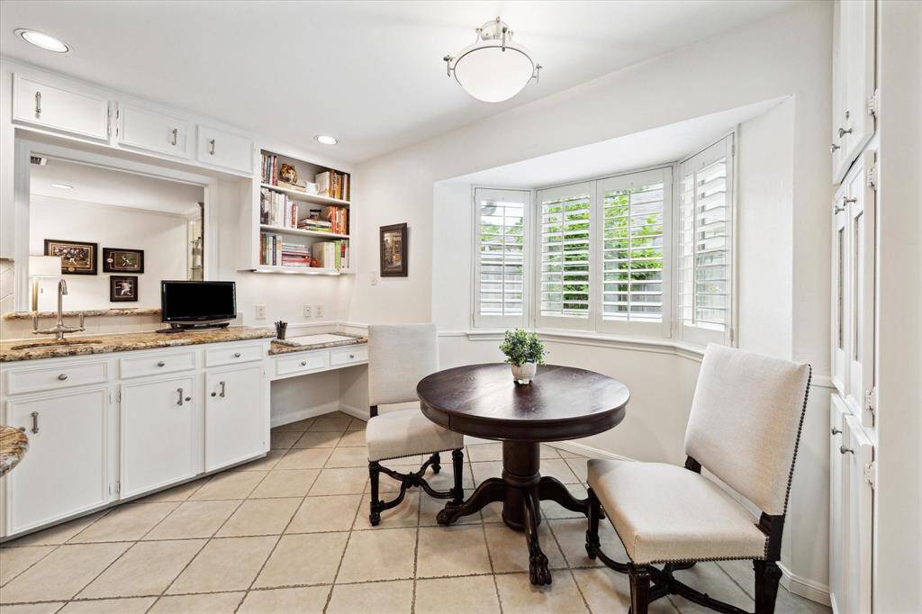 This cozy breakfast nook with room for a small table, surrounded by a bright bay window with plantation shutters. Adjacent is a built-in desk area with cabinetry, ideal for a small home office or study space.