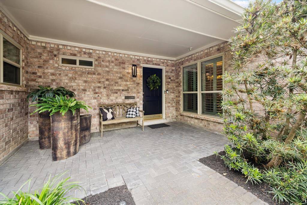 This charming and expansive covered front porch with brick walls and a welcoming black door create a warm and inviting entryway.