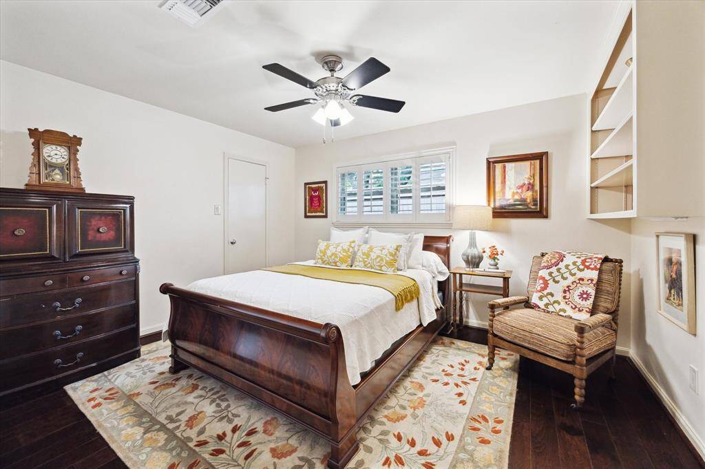 This cozy bedroom features a ceiling fan and warm lighting. The windows have wood shutters, creating a welcoming atmosphere.