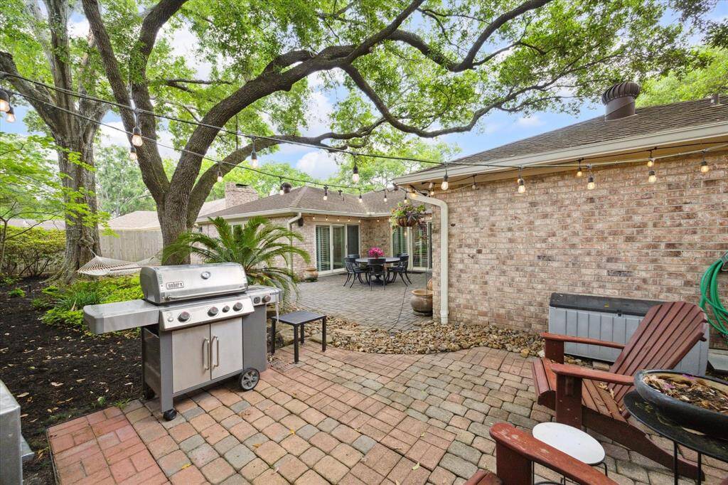 Charming backyard with a brick patio, string lights, and mature trees. Features a grilling and seating area, perfect for outdoor entertaining and relaxation.