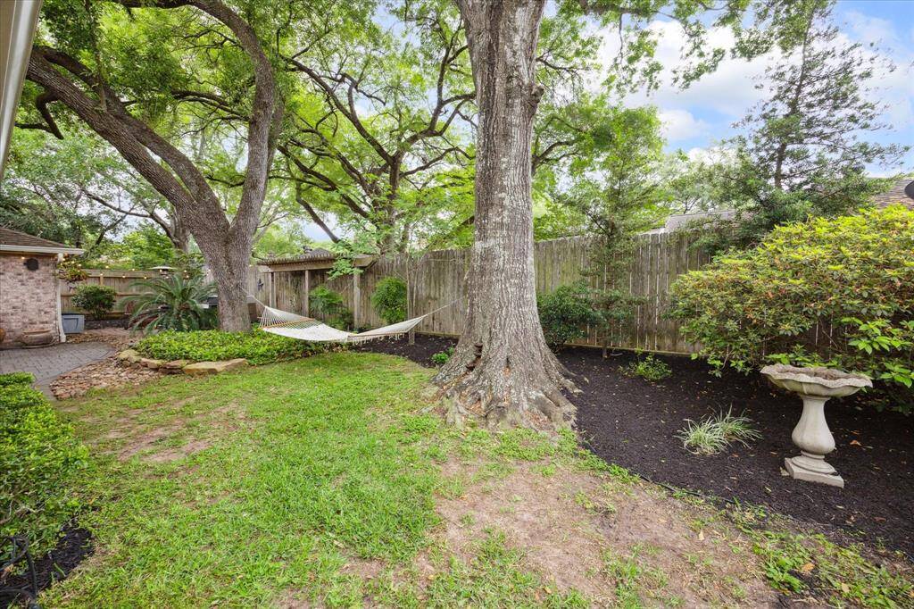 This inviting backyard features a large tree and lush greenery. A wooden fence provides privacy, creating a serene outdoor retreat.