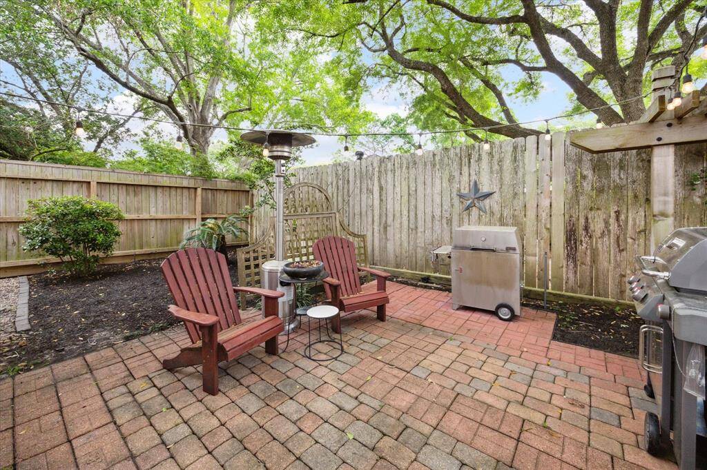 Additional seating area in this beautiful backyard with brick pavers. Perfect spot to grill on a nice evening and  surrounded by greenery and string lights, creating a perfect outdoor relaxation or entertainment space.