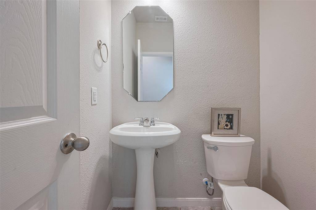 The powder room is appointed with a pedestal sink, wall-mounted mirror, and thoughtful lighting—perfectly placed for guests and quick fresh-ups.
