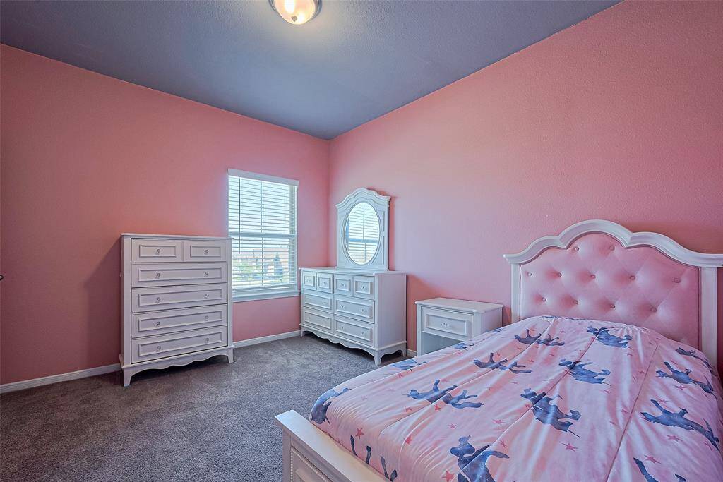 Bright and full of personality, this spacious bedroom is grounded in plush carpeting and energized by cheerful pink tones. A large window ensures the room feels open and welcoming.