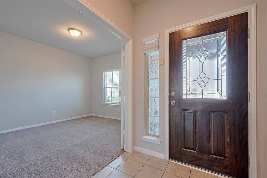 Step inside to a light-filled foyer with a glass-paneled front door and matching sidelight, casting natural light across the tile floor. To the right, elegant double doors open to a dedicated workspace.