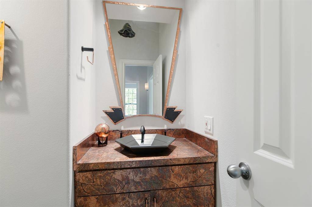 Downstairs half bathroom with a unique angular mirror and a stylish dark stone vessel sink set on a texture