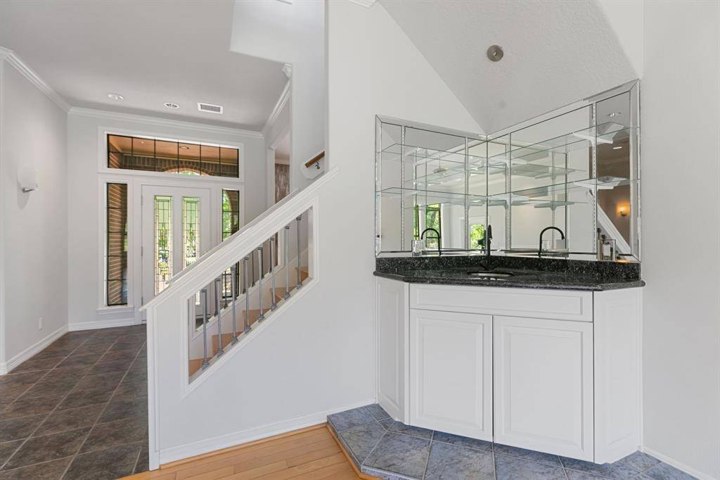 Bright entryway with tiled flooring, a staircase, and a mirrored wet bar with white cabinetry, creating a welcoming and functional space.