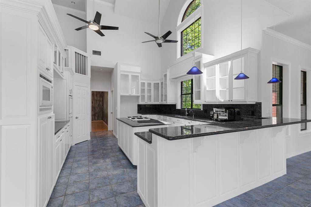 Kitchen features high ceilings, elegant white cabinetry, and sleek blue pearl granite countertops. It includes modern appliances, large windows for natural light, and stylish blue pendant lighting, creating a bright and contemporary cooking space.
