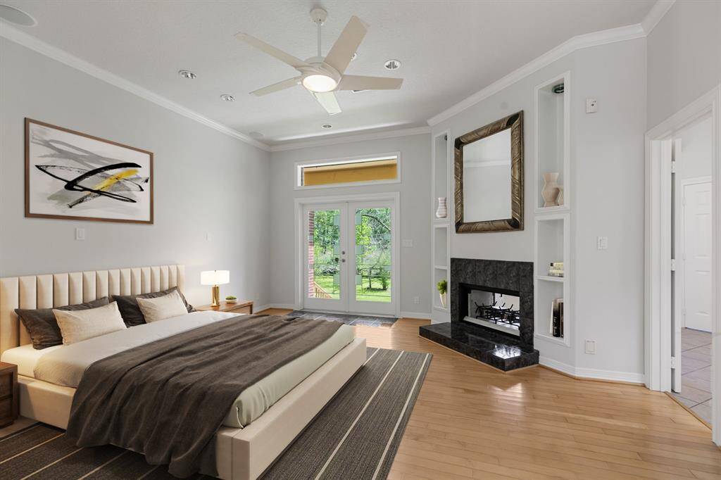 Virtually staged.  This spacious primary bedroom features a modern design with a fireplace and built-in shelving and ample natural light from the French doors leading to a wooded outdoor view.