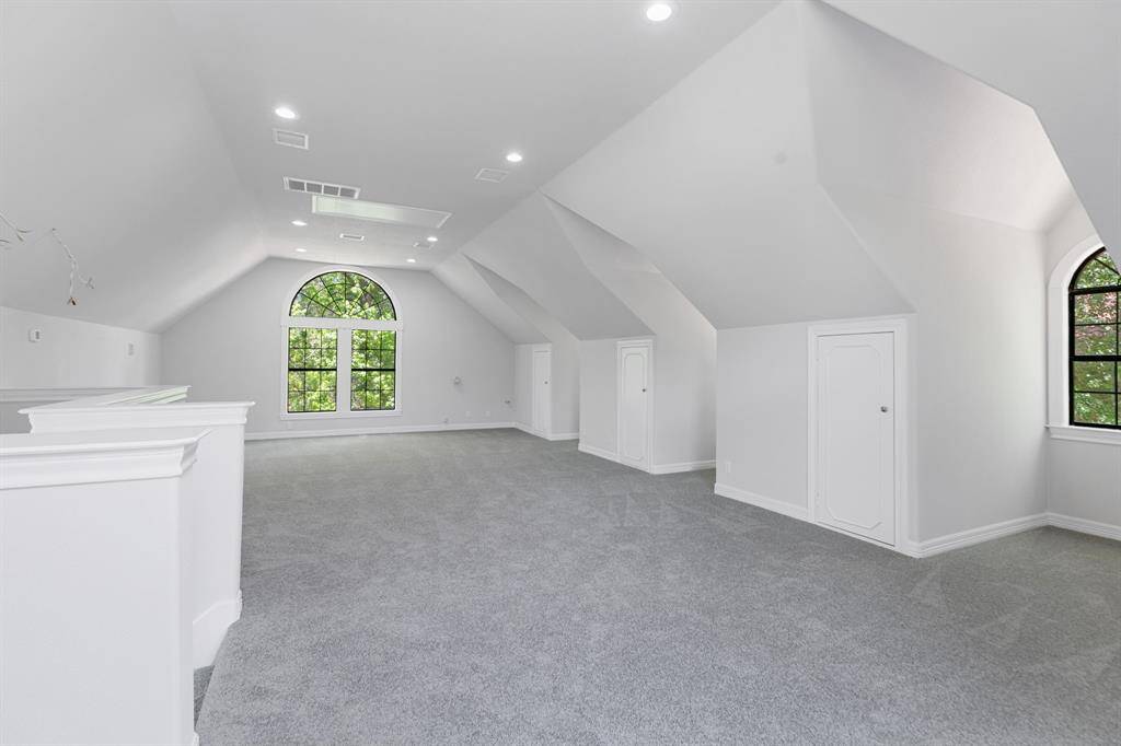 This spacious attic-style room features vaulted ceilings, plush carpeting, and ample natural light from large, arched windows, perfect for a versatile living space or gameroom, or apartment conversion.